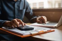 Foto: Person mit Taschenrechner und Laptop